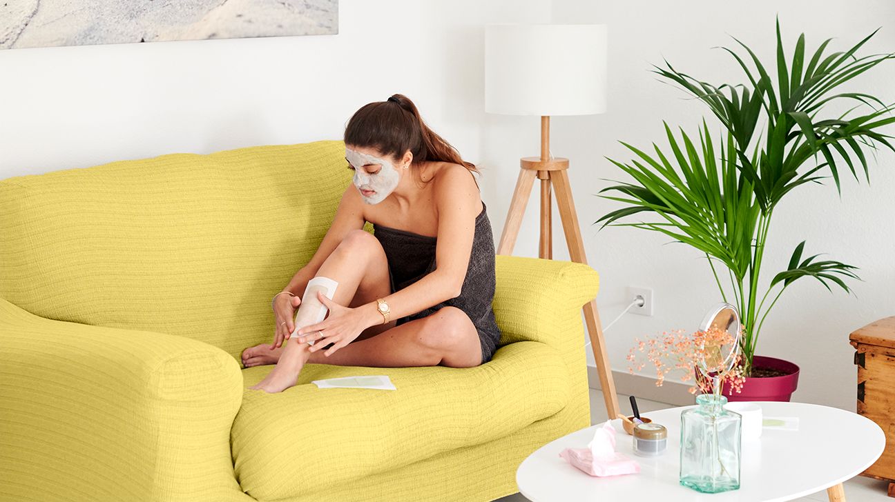 person waxing their legs at home on yellow couch